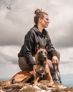 Svenja sitzt mit ihrem Malinois auf einem Felsen vor wolkigem Himmel