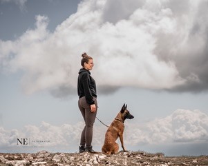 Svenja steht mit ihrem angeleinten Malinois auf einem Felsen unter großen Wolken