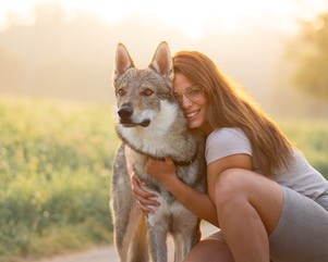 Svenja kniet im Morgenlicht auf einem Feldweg und umarmt ihren Wolfhund